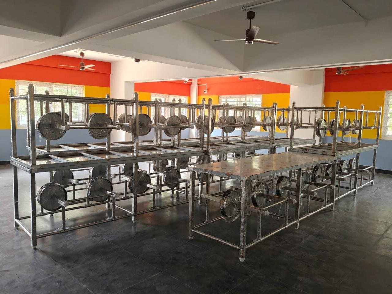 Rows of new stainless steel canteen dining tables with attached swivel seats in a Heritage Foods canteen hall