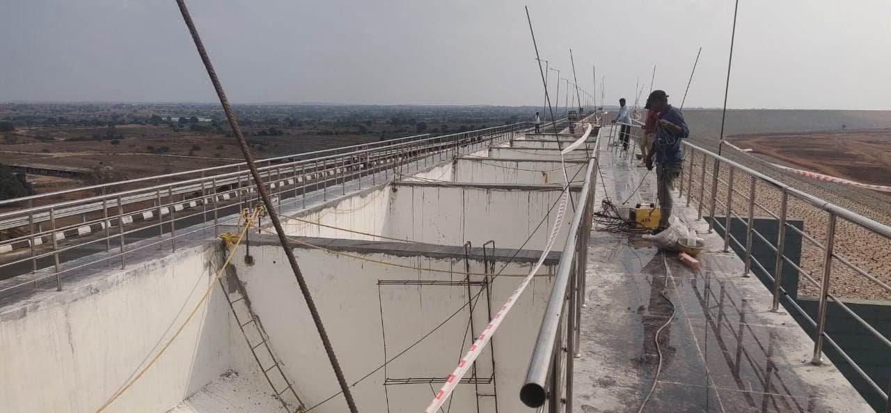 Workers welding stainless steel railing along the bridge beside open chambers